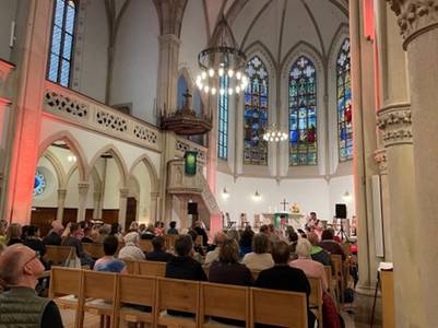 Innenraum der bunt beleuchteten Evangelischen Stadtkirche in Baden-Baden während des Aperol-Gottesdienstes am 13. September 2025. Die Besucher sitzen auf Holzbänken und blicken zum Altar, wo die junge Band der Petrusgemeinde Rastatt spielt.